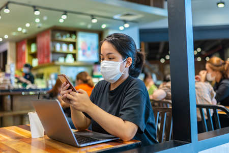 Woman wearing mask and using smartphone in cafeの写真素材
