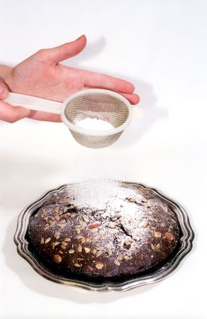 Powdered sugar sprinkling through sieve in woman hands to chocolate cakeの写真素材