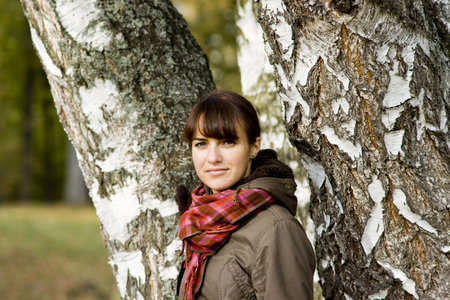 Pretty girl in warm coat near birches tree trunks looking at the cameraの写真素材