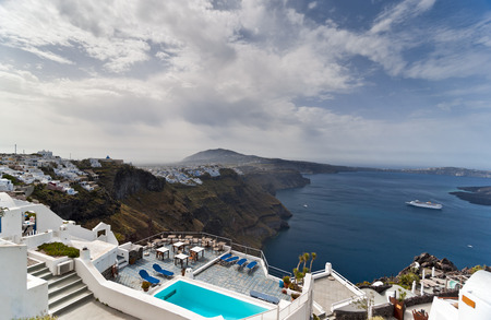 Santorini island and Caldera view with whitewashed houses, passenger vessel and swimming pool in frontの写真素材