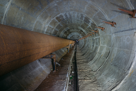 Old round dirty underground tunnel of heating duct with rusty pipelineの写真素材