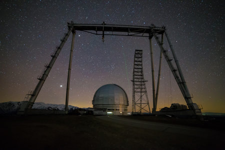Night view. A special astrophysical observatory and a crane against the background of the starry sky and snowy peaks of the Arkhyz mountains.の写真素材