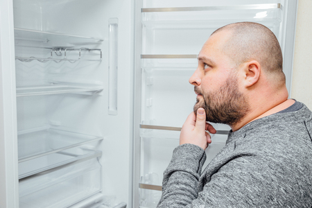 Fat hungry man is looking for a food into empty fridge.の写真素材