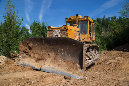 Big industrial yellow bulldozer leveling ground on road construction.