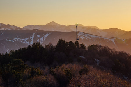 Antenna, radio tower on background of beautiful evening sunset at Caucasian mountains with snow...