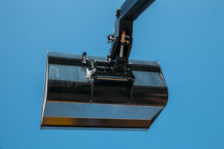 Black excavator bucket on blue sky background