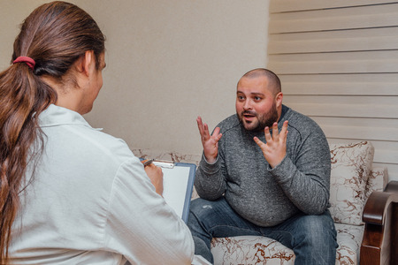 Doctor visits his patient. Sick sad man talking with doctor about his problems. Doctor writes notes.の写真素材
