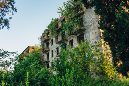 Ruined overgrown apartment house with bullet marks in ghost town, consequences of war in Abkhazia, green post-apocalyptic concept.の写真素材