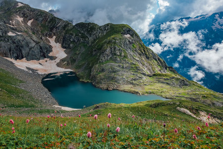 Cold small blue alpine Lake of Waning  Moon among flowers and clouds in summer, aerial view.