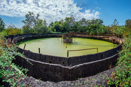 Abandoned wastewater treatment plant. Overgrown sewage purification tank with green water.