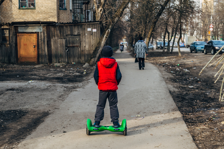 Boy on gyroscooter moves down the street of poor district, rear view.の写真素材