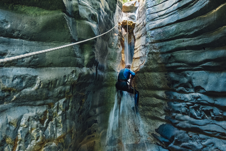 Waterfall rappelling. Man in wet suit climbs on waterfall in narrow river canyon.の写真素材