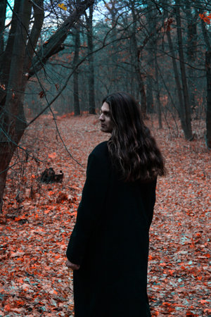 Brutal depressive Gothic stylish long haired man in autumn forest.