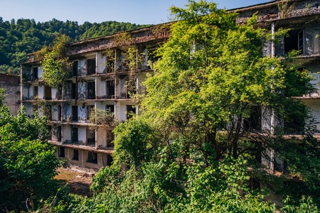 Ruined overgrown apartment house in ghost mining town, consequences of war in Abkhazia, green post-apocalyptic conceptの写真素材