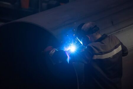 Worker in protective mask welding pipe in factory.の写真素材