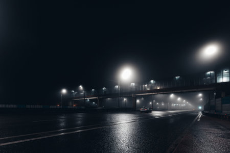 Foggy misty night road and overhead pedestrian bridge illuminated by street lights.
