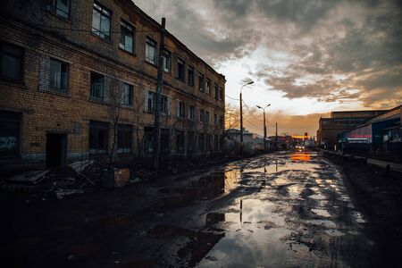 Old industrial area in evening. Dirty pools on cracked asphalt of damaged road.の写真素材