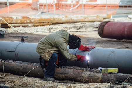 Repairing of city water supply or sewer pipeline. Worker is welding pipe.