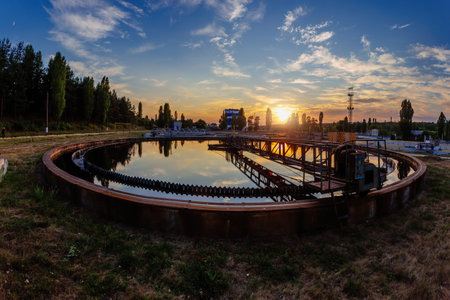 Modern sewage treatment plant. Round wastewater purification tanks at sunset, aerial view.