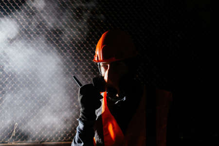 Man in respirator talking on walkie-talkie during fire in industrial buildingの写真素材