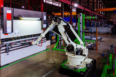 Robotic arm working with metal sheet at hydraulic bending machine.