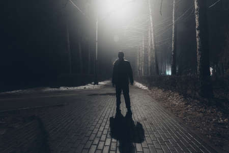 Sad man alone walking along the alley in the night foggy park.の写真素材