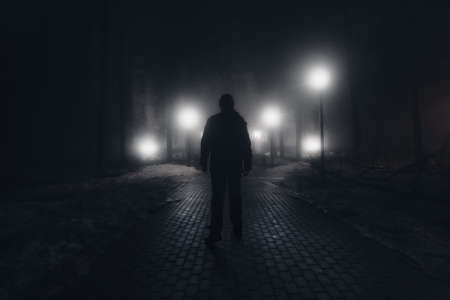 Sad man alone walking along the alley in the night foggy park.の写真素材