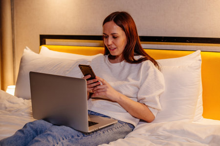 Young woman lying on the bed with laptop and mobile phone.の写真素材