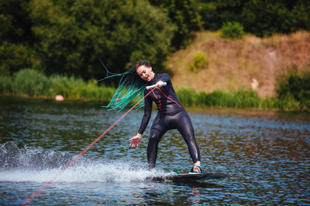A girl in a wetsuit stands on a wakeboard on the riverの写真素材