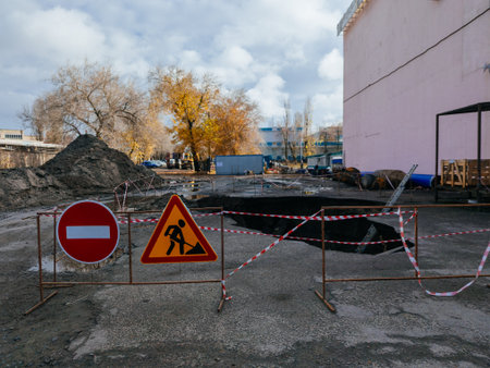 Collapsed asphalt. Large hole on urban road with warning symbols and signs.の写真素材