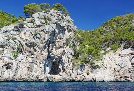 Beautiful cliff in the Mediterranean sea covered with green trees. Blue sky background. Spainの写真素材
