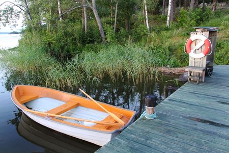 Empty white-orange fishing boat on a lake. Summer day. Sweden. Beautiful nature backgroundの写真素材