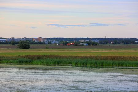 View on the city with big buildings and small houses from the river side. Sunset time.Green nature colors and blue sky with white clouds. Beautiful nature landscape backgrounds.の写真素材