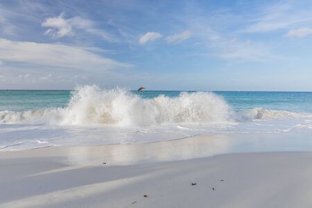 Big wave in Caribbean sea is breaking the coast. Turquoise sea water and blue sky. Eagle Beach of Aruba Island. Beautiful nature background.の写真素材