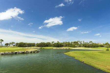 Beautiful tropical natural landscape view. Green grass field and pond water surface on blue sky with rare white clouds background.の写真素材