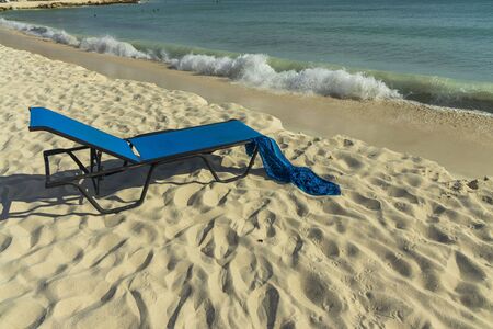 Gorgeous view of blue sun bed with forgotten blue scarf on white sand beach. Coast line on turquoise water and blue sky background. Atlantic Ocean. Aruba island.の写真素材