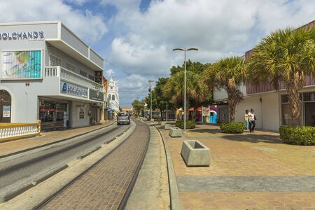 Beatiful view of one of streets of Oranjestad. Buildings and green trees along tram rails on blue sky with white clouds backgrounds. Oranjestad. Aruba, 09/13/2019.のeditorial素材