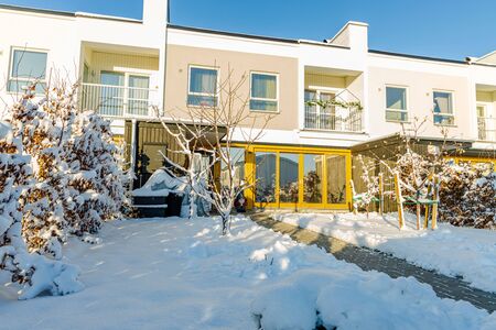 Beautiful exterior view of townhouses with front yard covered with snow. White and yellow on blue sky background.の写真素材