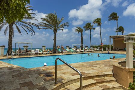 View of tourists taking sun shower at pool of Tamarijn hotel. Turquoise water on blue sky background. Oranjestad. Aruba. 15/09/2019.のeditorial素材