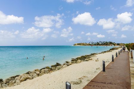 Beautiful view of white sand Aruba beach. Blue sunbeds under sun umbrellas on turquoise water and blue sky with white clouds background. Caribbean. Atlantic ocean. Oranjestad. Aruba.のeditorial素材