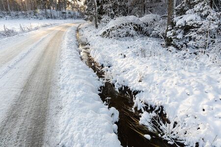 Beautiful view of winter scape. Country road and stream in snow forest. Trees reflection on water. Winter time in Sweden.の写真素材