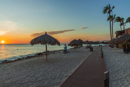 Beautiful view of coast line hotel area on sunset. White sand beach. sun umbrellas and palm trees on blue sky background. Tamarijn hotel.Oranjestad. Aruba. 17/09/2019のeditorial素材