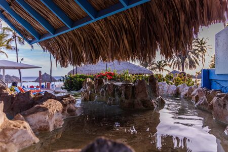 Beatiful view of decorative pool on coast of Atlantic ocean. Green plants and sun umbrellas on blue sky background. Willemstad. Curacao.の写真素材