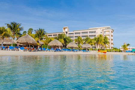 Beautiful view of white sand Curacao beach. Blue sunbeds under sun umbrellas on turquoise water and blue sky with white clouds background. Curacao Island. Beautiful backgrounds.のeditorial素材