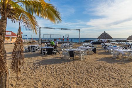 View over hotel beach being prepared for evening performance. Round tables covered with white clothes on blue sky with white clouds background. Willemstad. Curacao.のeditorial素材