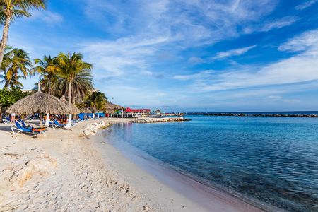Beautiful view of white sand Curacao beach. Blue sunbeds under sun umbrellas on turquoise water and blue sky with white clouds background. Curacao Island. Beautiful backgrounds.のeditorial素材