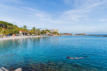 Beautiful ocean landscape view. Tourists swimming in turquoise water of Atlantic Ocean. Sand beach and palm trees on blue sky background. Willemstad. Curacao.のeditorial素材
