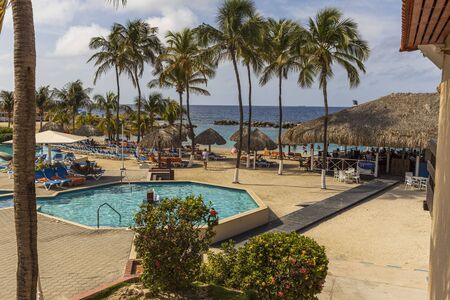 Beautiful view of hotel area. Outdoor pool with blue sun beds and umbrellas on green palm trees background. Willemstad. Curacao. 09/09/2019.のeditorial素材