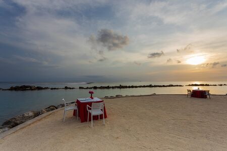 Gorgeous view of two romantic decorated tables on white sand beach on sunset. Turquoise water of Atlantic ocean merging with blue sky on background. Willemstad. Curacao.の写真素材
