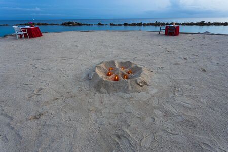 Beautiful view of two romantic decorated tables on white sand beach. Turquoise water of Atlantic ocean merging with blue sky on background. Willemstad. Curacao.の写真素材
